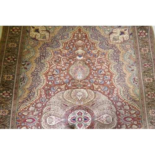 1105 - A Turkish Hereke wool carpet with central design on a faded terracotta field, with blue/grey borders... 