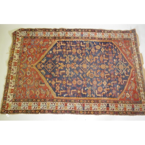 1018 - An antique Persian hand woven wool carpet, with medallion design on a red and blue field with ivory ... 