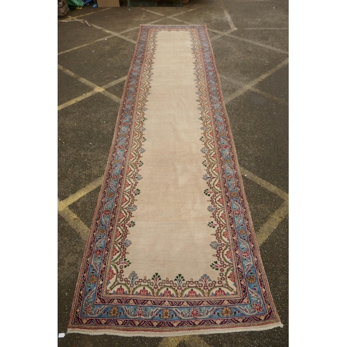 1033 - An Oriental cream ground hand woven wool runner with blue border and floral designs, 150 x 600cm