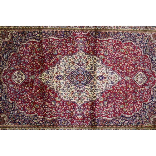 1077 - A red ground Kashmir rug with traditional floral medallion design and blue borders, 170 x 120cm