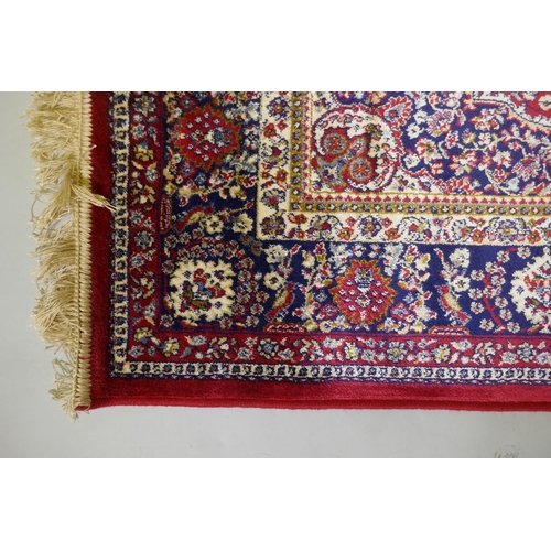 1077 - A red ground Kashmir rug with traditional floral medallion design and blue borders, 170 x 120cm