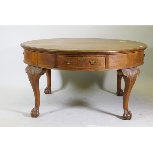 1120 - A Georgian style oak library/drum table with four drawers, raised on cabriole supports with carved d... 