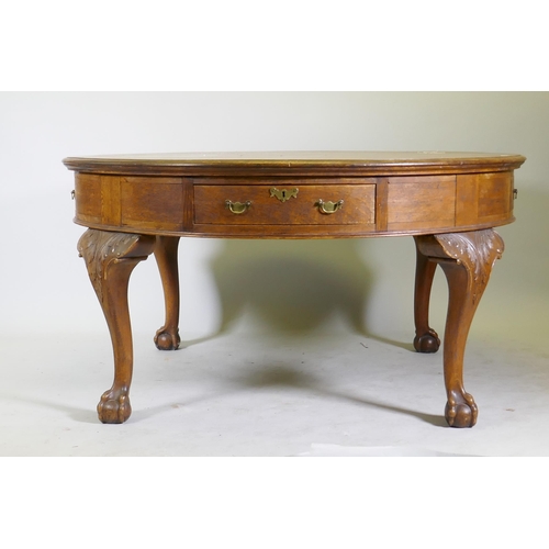 1120 - A Georgian style oak library/drum table with four drawers, raised on cabriole supports with carved d... 