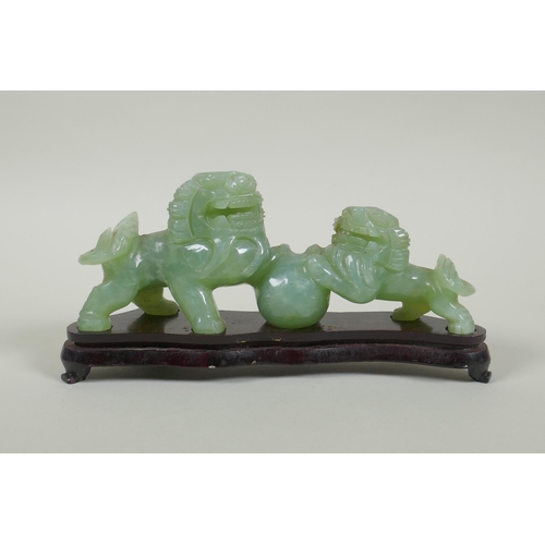 115 - A Chinese celadon jade carving of twin fo-dogs, on a lacquered wood stand, 21cm long