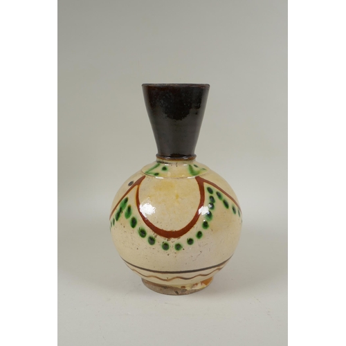 179 - An antique Islamic earthenware vase with cream glazed body and treacle glazed neck, 25cm high