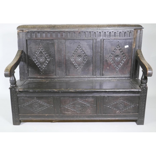 1007 - An C18th oak settle with carved panel back and front, lift up seat, raised on stile supports, with a... 