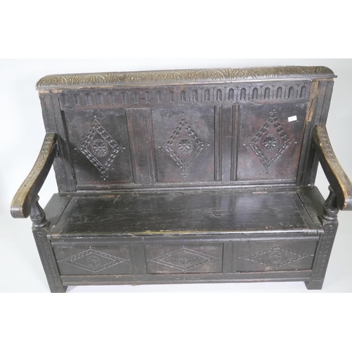 1007 - An C18th oak settle with carved panel back and front, lift up seat, raised on stile supports, with a... 