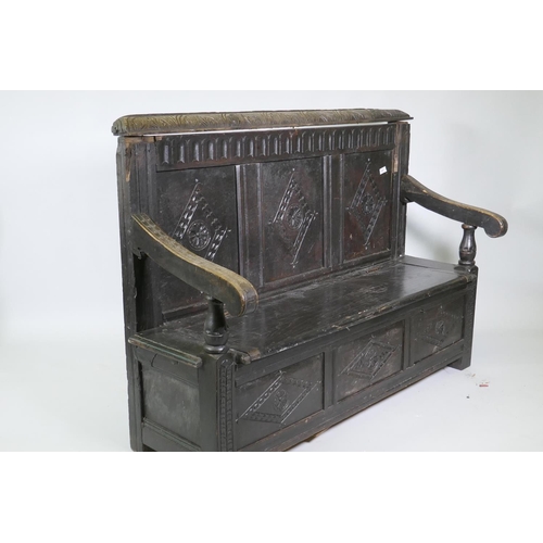 1007 - An C18th oak settle with carved panel back and front, lift up seat, raised on stile supports, with a... 