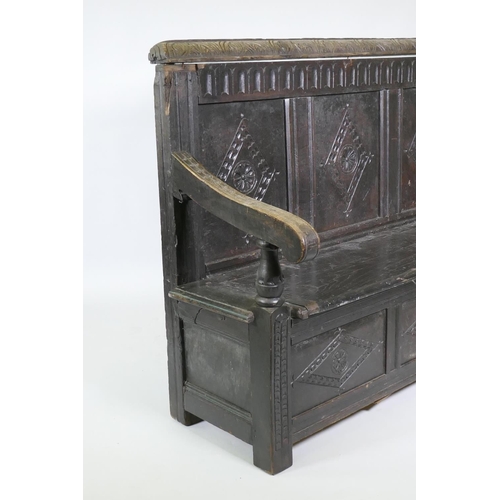 1007 - An C18th oak settle with carved panel back and front, lift up seat, raised on stile supports, with a... 