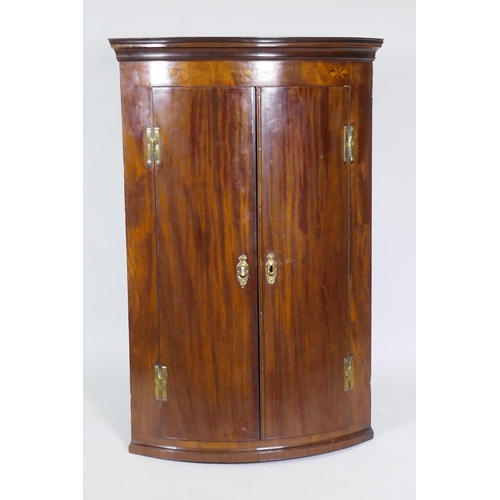 1018 - A Georgian mahogany bow fronted hanging corner cupboard, with inlaid decoration, H hinges and decora... 