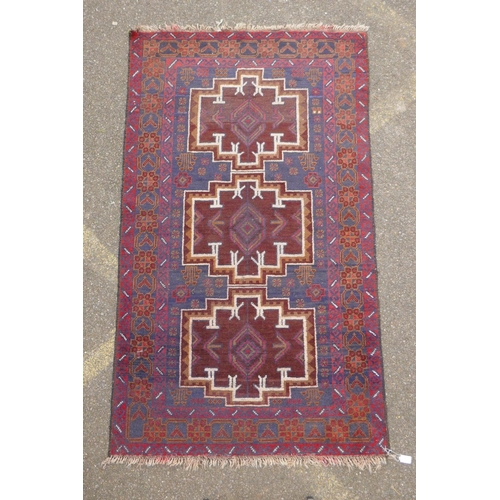 1039 - A Persian Baluch red and blue wool rug decorated with two geometric medallions, 104 x 180cm