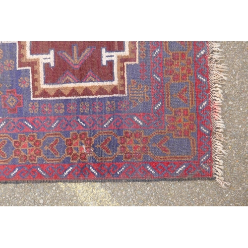 1039 - A Persian Baluch red and blue wool rug decorated with two geometric medallions, 104 x 180cm