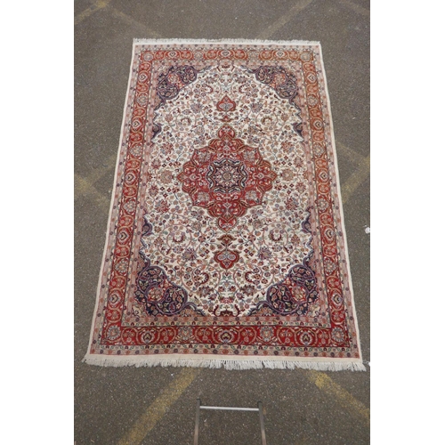 1052 - A Persian ivory ground wool Tabriz carpet with a floral medallion and red borders, 180 x 284cm