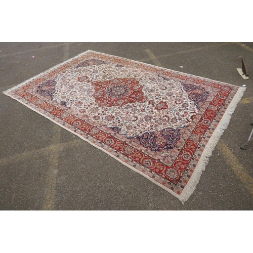 1052 - A Persian ivory ground wool Tabriz carpet with a floral medallion and red borders, 180 x 284cm