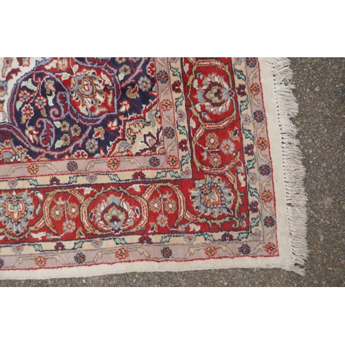 1052 - A Persian ivory ground wool Tabriz carpet with a floral medallion and red borders, 180 x 284cm