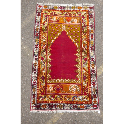 1058 - A rich red ground Caucasian rug with prayer mat design and multi-colour borders, 112 x 186cm