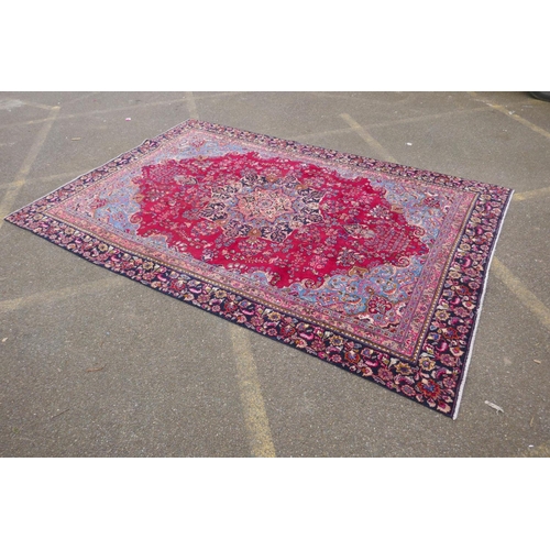 1065 - A claret and blue ground Persian Mashad carpet with a traditional floral medallion design, patched, ... 