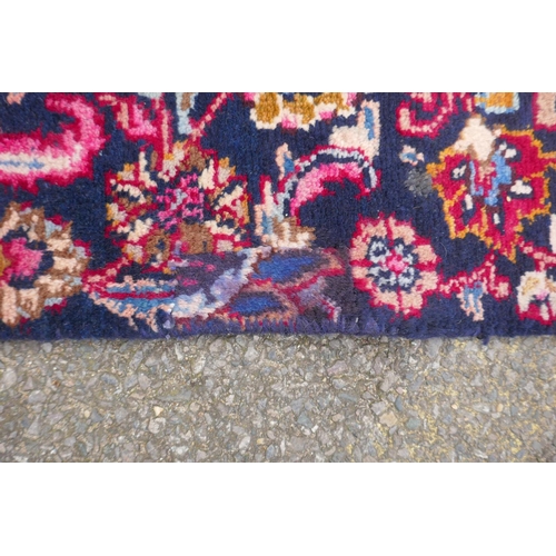 1065 - A claret and blue ground Persian Mashad carpet with a traditional floral medallion design, patched, ... 