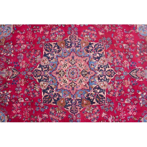 1065 - A claret and blue ground Persian Mashad carpet with a traditional floral medallion design, patched, ... 