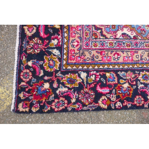 1065 - A claret and blue ground Persian Mashad carpet with a traditional floral medallion design, patched, ... 