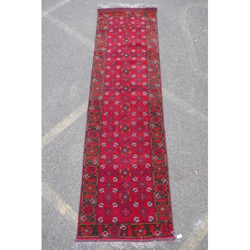 1082 - A rich red ground Persian wool runner with an allover geometric design and black borders, 84 x 290cm