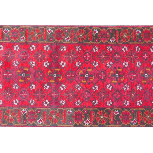 1082 - A rich red ground Persian wool runner with an allover geometric design and black borders, 84 x 290cm