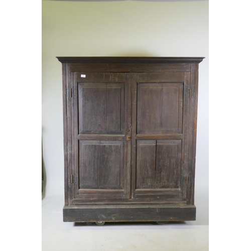 1101 - An early C18th two door cupboard with fielded panel doors and panelled sides, raised on a plinth bas... 