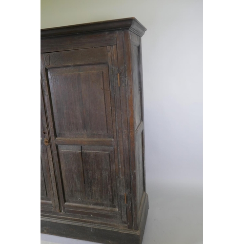 1101 - An early C18th two door cupboard with fielded panel doors and panelled sides, raised on a plinth bas... 