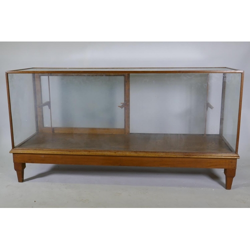 1111 - An oak framed glass shop cabinet with two sliding doors, raised on turned supports, 178  x 58 x... 