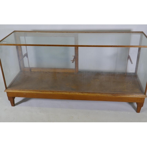 1111 - An oak framed glass shop cabinet with two sliding doors, raised on turned supports, 178  x 58 x... 