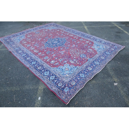 1139 - A large Persian red ground wool carpet with floral medallion design and blue borders, some wear, 74 ... 