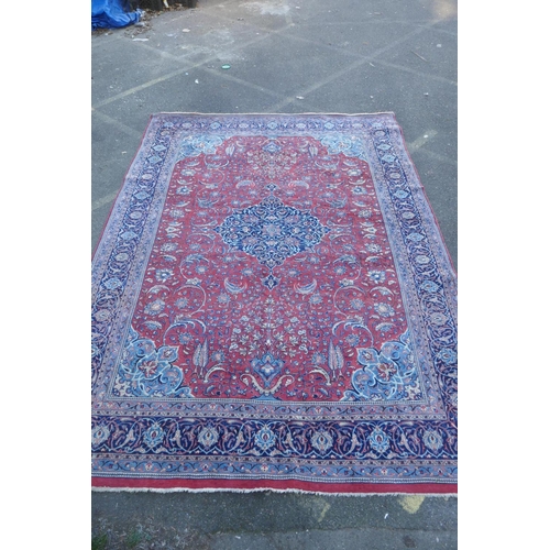 1139 - A large Persian red ground wool carpet with floral medallion design and blue borders, some wear, 74 ... 