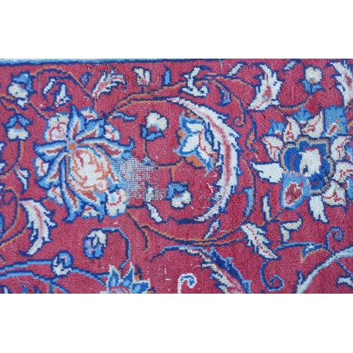 1139 - A large Persian red ground wool carpet with floral medallion design and blue borders, some wear, 74 ... 