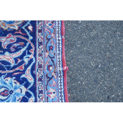 1139 - A large Persian red ground wool carpet with floral medallion design and blue borders, some wear, 74 ... 