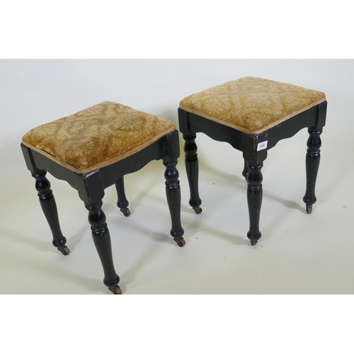 1196 - A pair of Victorian ebonised stools, with shaped friezes, raised on turned supports with metal casto... 