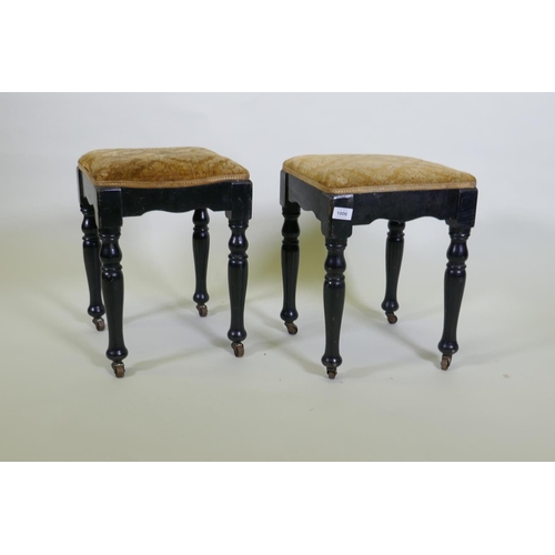 1196 - A pair of Victorian ebonised stools, with shaped friezes, raised on turned supports with metal casto... 