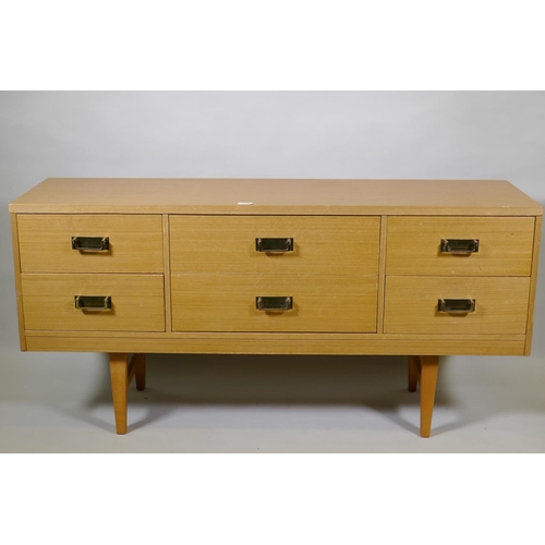 1019 - A mid century faded sapele six drawer chest with brass handles, raised on square tapering supports, ... 