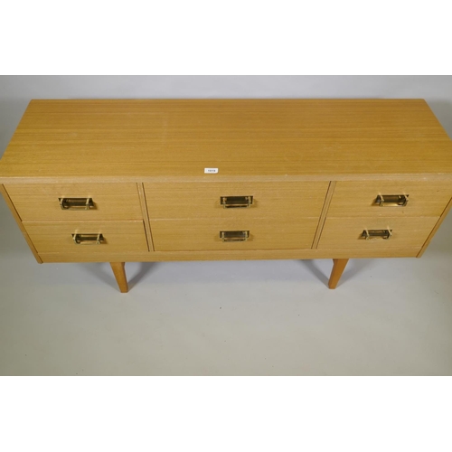 1019 - A mid century faded sapele six drawer chest with brass handles, raised on square tapering supports, ... 