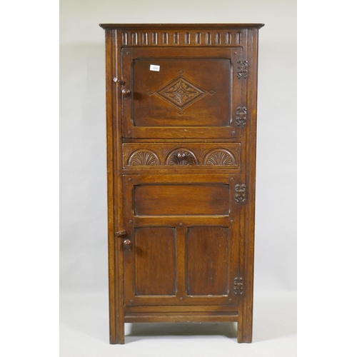 1050 - A mid century oak hall cupboard with panelled sides and doors and carved decoration, two cupboards w... 