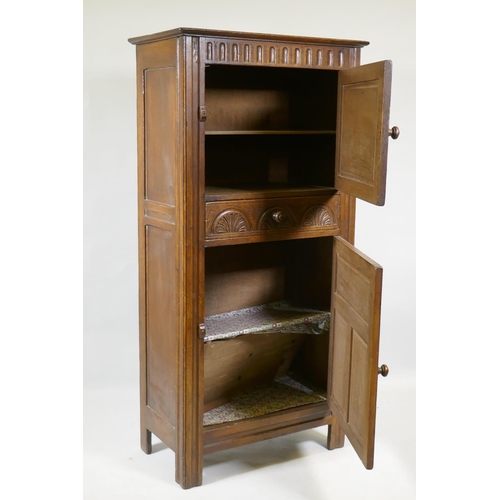 1050 - A mid century oak hall cupboard with panelled sides and doors and carved decoration, two cupboards w... 