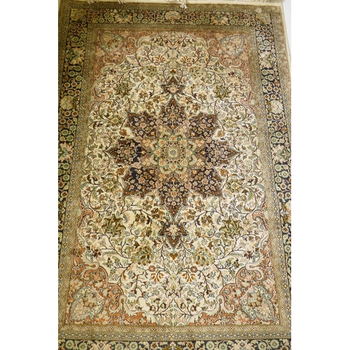 1180 - An Oriental silk carpet with floral designs and central medallion on a cream and faded terracotta fi... 