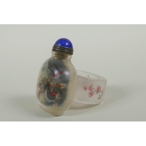 135 - A Chinese reverse decorated glass snuff bottle on a ring, decorated with a green dragon and a red le... 