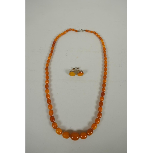 634 - A vintage graduated butterscotch amber necklace and a pair of matching earrings with silver gilt mou... 