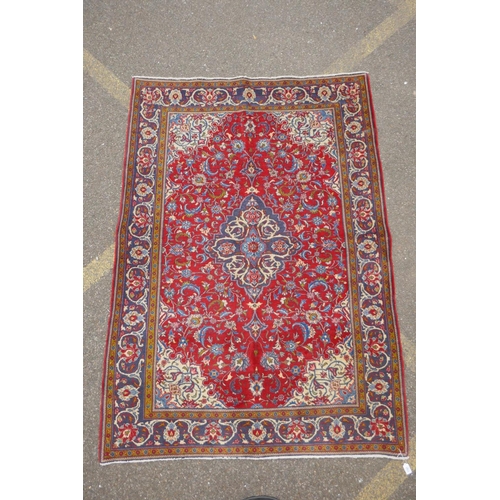 1151 - A Persian red ground Kashan carpet with floral medallion design and blue borders, 140 x 196cm