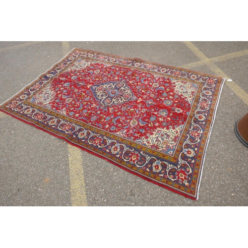 1151 - A Persian red ground Kashan carpet with floral medallion design and blue borders, 140 x 196cm