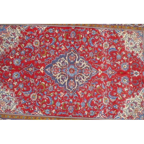 1151 - A Persian red ground Kashan carpet with floral medallion design and blue borders, 140 x 196cm