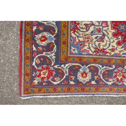 1151 - A Persian red ground Kashan carpet with floral medallion design and blue borders, 140 x 196cm