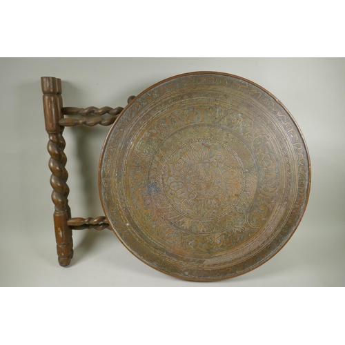 1172 - A Persian brass tray table on a folding base, with engraved Islamic script decoration, 60cm diameter... 