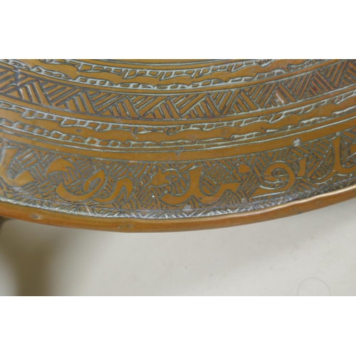 1172 - A Persian brass tray table on a folding base, with engraved Islamic script decoration, 60cm diameter... 