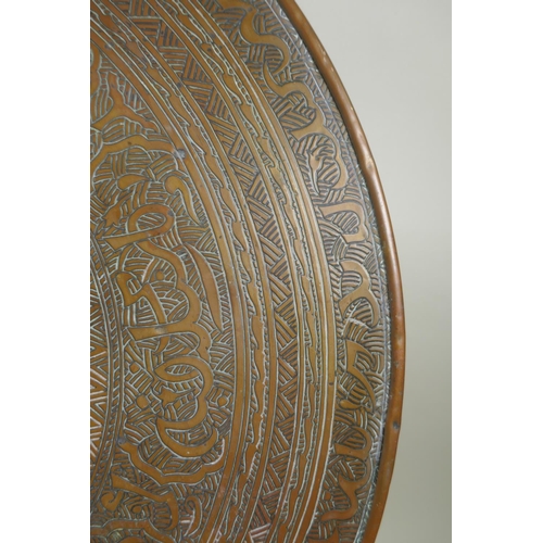 1172 - A Persian brass tray table on a folding base, with engraved Islamic script decoration, 60cm diameter... 